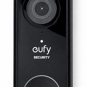 May include: Black eufy Security video doorbell with a camera lens, the brand name, and a circular button. The top has a small section with an arrow. The doorbell is rectangular and mounted on a white background.