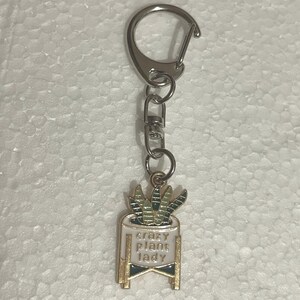May include: A gold-colored keychain with a white pot and green plant. The pot has the text "crazy plant lady" on it.