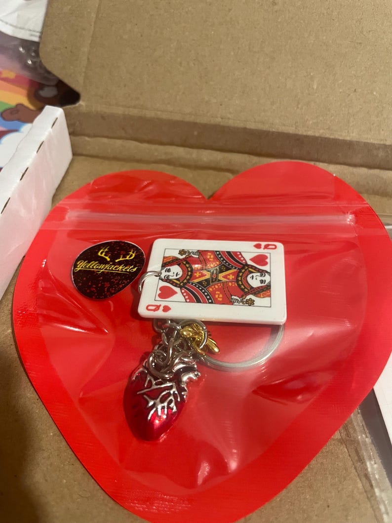 Puede incluir: Un llavero con una carta de la Reina de Corazones y un dije de coraz&oacute;n anat&oacute;mico rojo. El llavero est&aacute; sujeto a un llavero plateado. Los art&iacute;culos est&aacute;n empaquetados en una bolsa de pl&aacute;stico roja en forma de coraz&oacute;n con una pegatina amarilla que dice "Yellowjackets".