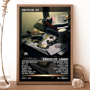 May include: A framed rectangular poster featuring the Section.80 album cover by Kendrick Lamar. The artwork displays a dark, cluttered table with a gold chain, a pipe, and a pill bottle. The text includes the artist name, tracklist, and date.