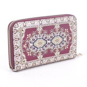 May include: A rectangular wallet featuring a deep burgundy background with a detailed, intricate cream and dark-toned floral pattern reminiscent of a woven rug. The wallet is secured with a metallic zipper that runs along the top and side edges.