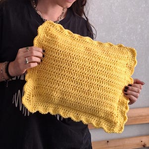 Peut inclure: Un coussin jaune au crochet fait à la main, avec un bord festonné. Le coussin est rectangulaire et semble doux et confortable. Les points de crochet sont visibles. Idéal pour la décoration intérieure.