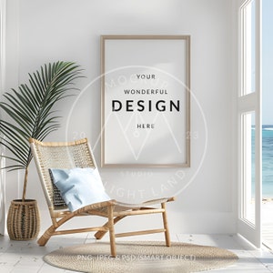 May include: A light wood framed poster mockup with the text "Your Wonderful Design Here" in a white room with a wicker chair and a potted palm plant. The chair has a light blue pillow and is sitting on a white rug. A window with a view of the ocean is in the background.