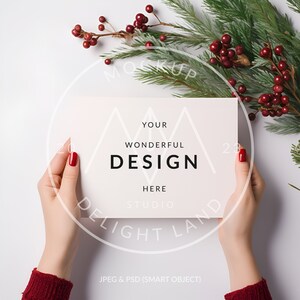 May include: A white card with the text "YOUR WONDERFUL DESIGN HERE STUDIO" in black text. The card is held by hands with red nail polish against a white background with a green pine branch and red berries.