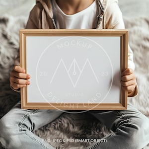 May include: A child holds a wooden framed picture with a white background. The frame has a white circle with the text "MOCKUP 20 STUDIO DELIGHT LAND 23" in it.