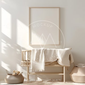 May include: A white wooden frame mockup with a blank canvas, hanging on a white wall. A wicker crib with a white blanket is in the foreground. The crib is next to a wicker basket with a stuffed animal inside. The room is decorated in a minimalist style with natural light.