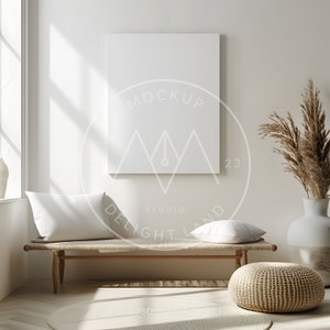May include: A white canvas mockup hanging on a white wall above a wooden bench with two white pillows and a woven ottoman. A vase with dried pampas grass is on the right side of the image. The text "MOCKUP" is visible on the canvas.