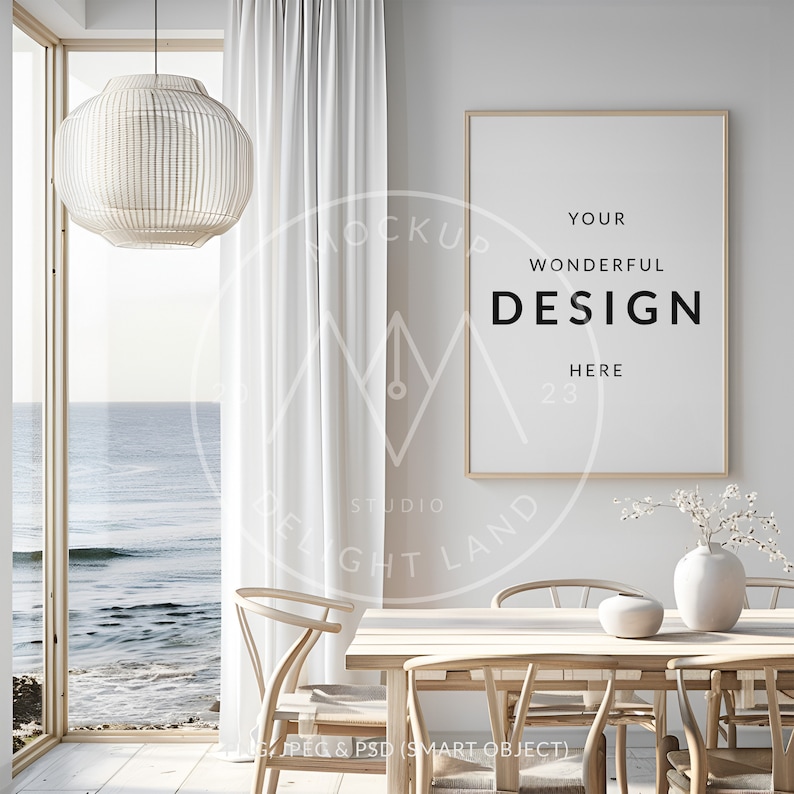 May include: A framed poster mockup with the text "YOUR WONDERFUL DESIGN HERE 23" hanging on a white wall in a coastal-themed dining room. The room features a wooden table with chairs, a white vase with dried branches, and a large window with an ocean view.