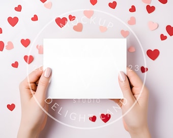 Puede incluir: Una tarjeta blanca sostenida por manos sobre un fondo de corazones rosas y rojos. La tarjeta está en blanco y lista para un mensaje.