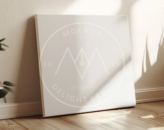 Könnte beinhalten: Ein weißer Leinwand-Mockup mit einem Logo, das "MOCKUP STUDIO DELIGHT LAND" mit einem Berg- und Stiftdesign sagt. Die Leinwand lehnt an einer weißen Wand mit einem Schatten aus einem Fenster.