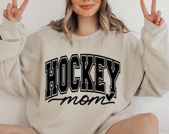 May include: A light beige sweatshirt with the text "HOCKEY MOM" in black with a small heart next to the word "MOM".