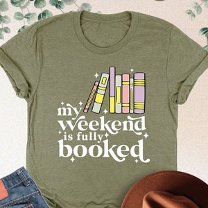 May include: A green t-shirt with a white graphic that says "my weekend is fully booked" with a stack of colorful books and stars.