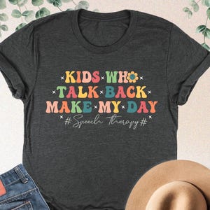 May include: Dark heather grey t-shirt with a rainbow design that says "KIDS WHO TALK BACK MAKE MY DAY #Speech Therapy#"
