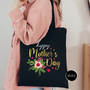 a woman holding a black tote bag that says happy mother's day