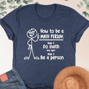 May include: A navy blue t-shirt with a white stick figure illustration and the text "How to be a MATH PERSON: Step 1: Do math (any type) Step 2: Be a person"