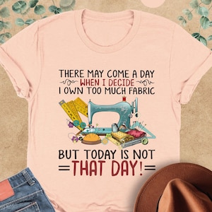 May include: A pink t-shirt with a sewing machine and sewing supplies graphic. The text on the shirt reads "There may come a day when I decide I own too much fabric but today is not =that day!="