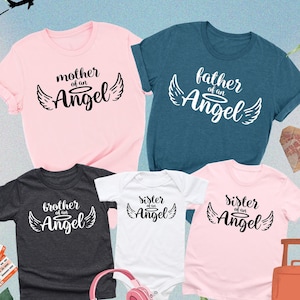 Op de afbeelding: Een set van vijf t-shirts met de tekst "moeder van een engel", "vader van een engel", "broer van een engel" en "zus van een engel" erop gedrukt. De shirts zijn in de kleuren roze, teal, grijs, wit en roze.