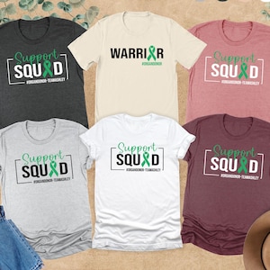 May include: Five different color t-shirts with the text "Support Squad" and a green ribbon. The text "#ORGANDONOR-TEAMASHLEY" is below the text "Support Squad". One t-shirt has the text "Warrior" with the text "#ORGANDONOR" below it.