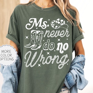 May include: A moss green t-shirt with the text "Ms. never do no Wrong" in white script, along with illustrations of cowboy boots and a hat. The shirt has rolled-up sleeves and is part of a casual wear collection.