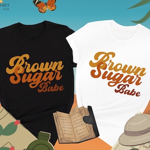 May include: Two t-shirts with the text "Brown Sugar Babe" in a retro font. The shirts are black and white with orange and brown text.