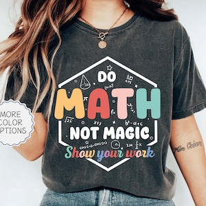 May include: Dark gray t-shirt with a colorful graphic that reads "DO MATH NOT MAGIC" in a hexagon shape. The design includes math symbols and the phrase "Show your work". The shirt has a vintage, worn look.