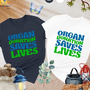 May include: Two t-shirts with the text "Organ Donation Saves Lives" in green and blue letters on a white and heather navy background.