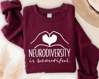 May include: Maroon sweatshirt with white text that reads "Neurodiversity is beautiful". The text is accompanied by a graphic of two hands forming a heart shape.
