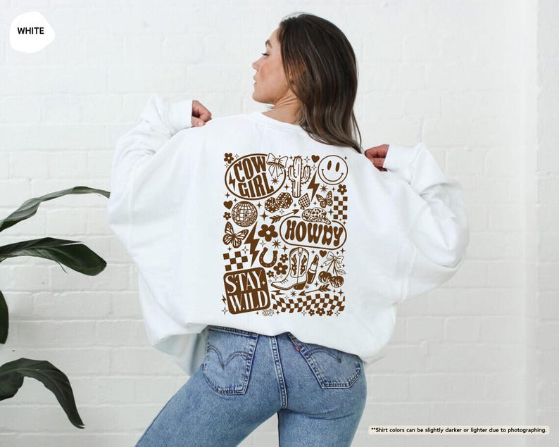 K&ouml;nnte beinhalten: Wei&szlig;es Sweatshirt mit braunem Grafikdesign auf dem R&uuml;cken. Das Design enth&auml;lt die W&ouml;rter "COW GIRL", "HOWDY" und "STAY WILD" sowie Bilder von Kaktus, Stiefeln, einem Smiley und anderen Elementen im Western-Stil.