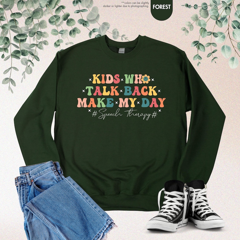 May include: A dark green sweatshirt with the text "KIDS WHO TALK BACK MAKE MY DAY #Speech therapy#" in rainbow colors.