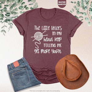 May include: A heather maroon t-shirt with the text "The Little Voices In My Head Keep Telling Me Get More Yarn" and a graphic of a ball of yarn with knitting needles.