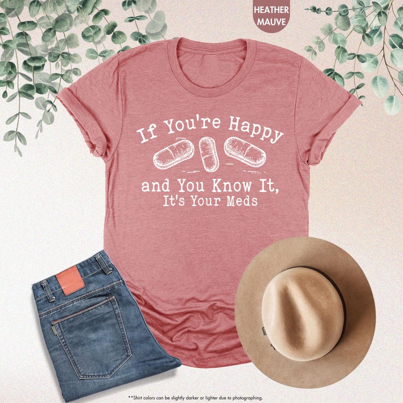 May include: Heather mauve t-shirt with the text "If You're Happy and You Know It, It's Your Meds" in white. The shirt features a graphic of three white pills.