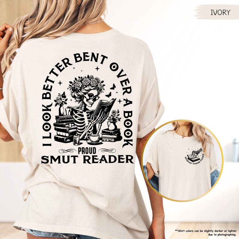 May include: A white t-shirt with black text that reads 'I look better bent over a book, Proud Smut Reader.' The shirt features a black and white illustration of a skeleton reading a book. The shirt is displayed on a model with a light brown background.