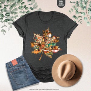 Puede incluir: Una camiseta gris oscuro jaspeado con un gr&aacute;fico de hoja de arce compuesto por varios patrones de patchwork con tem&aacute;tica oto&ntilde;al, incluyendo calabazas, girasoles y cuadros, junto a unos vaqueros azules y un sombrero fedora de fieltro.