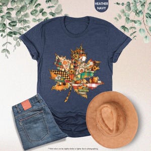 Puede incluir: Una camiseta de manga corta en azul marino jaspeado con un gr&aacute;fico de hoja de arce compuesto por varios patrones oto&ntilde;ales, incluyendo calabazas, girasoles y cuadros, presentada junto a unos vaqueros azules y un sombrero de fieltro color canela.