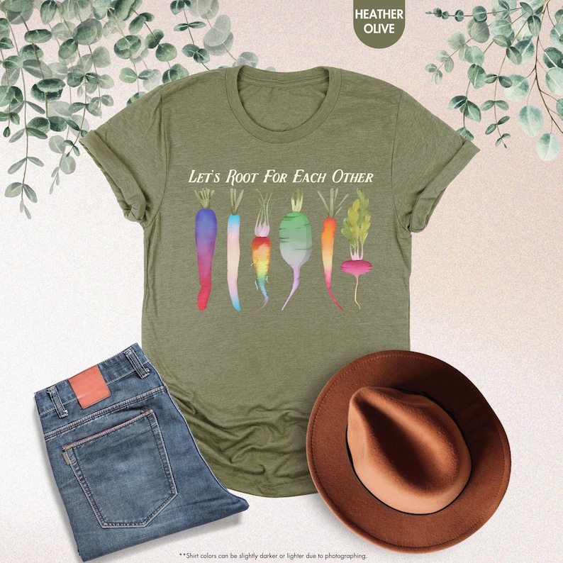 May include: A green t-shirt with the text "Let's Root For Each Other" and a graphic of colorful carrots and radishes. The shirt is available in heather olive.