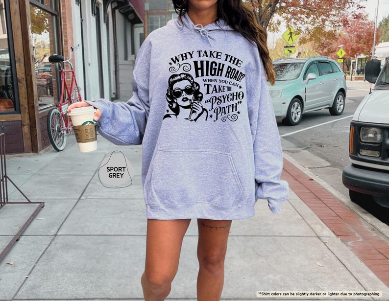 May include: A light grey hoodie with a graphic that reads "WHY TAKE THE HIGH ROAD WHEN YOU CAN TAKE THE PSYCHO PATH." The graphic features a woman in sunglasses. The hoodie is labeled "SPORT GREY".