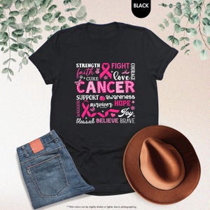 a t - shirt with a pink ribbon and a hat next to it