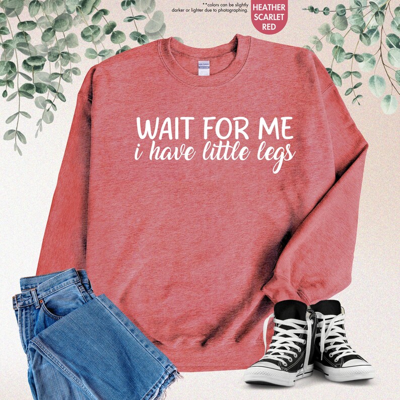 Pode incluir: Camisola vermelha escarlate mesclada com o texto "WAIT FOR ME i have little legs" em branco. A imagem tamb&eacute;m mostra cal&ccedil;as de ganga azuis e t&eacute;nis pretos e brancos.
