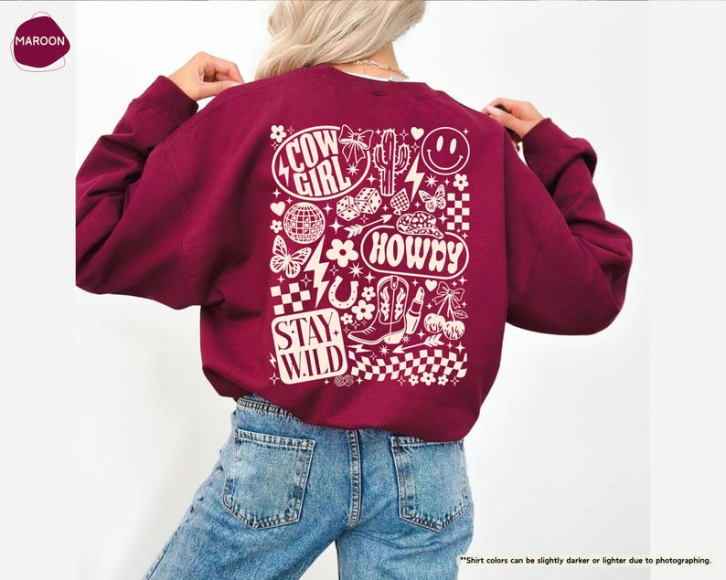 K&ouml;nnte beinhalten: Ein weinrotes Sweatshirt mit einem wei&szlig;en Grafikdesign auf dem R&uuml;cken. Das Design enth&auml;lt die W&ouml;rter "Cow Girl", "Howdy" und "Stay Wild" sowie Bilder von Kaktus, Stiefeln, Schmetterlingen und einem Smiley.