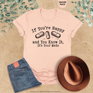 May include: A pink t-shirt with the text "If You're Happy and You Know It, It's Your Meds" and a graphic of three pills.