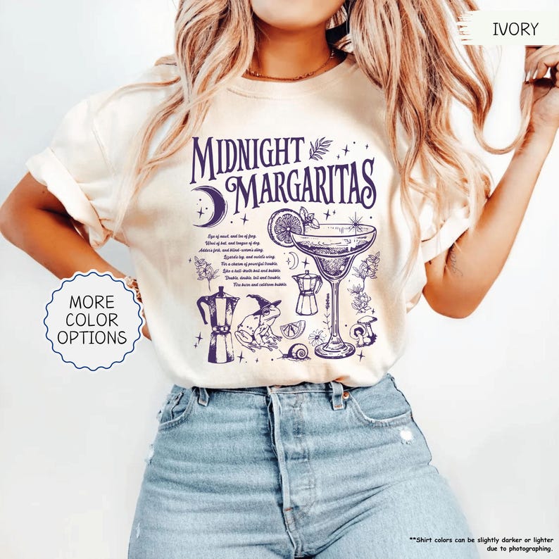 May include: Ivory-colored t-shirt with the text "MIDNIGHT MARGARITAS" in dark blue. The design includes a cocktail glass, a crescent moon, and other illustrations. The shirt also has the words "MORE COLOR OPTIONS" on it.