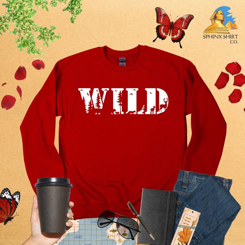 May include: Red long-sleeve sweatshirt with the word "WILD" in white letters. The letters are made up of silhouettes of trees, animals, and other nature elements.
