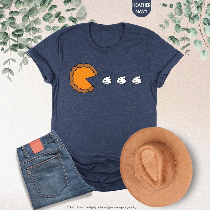 May include: A heather navy blue t-shirt with a graphic of a pumpkin pie with a bite taken out of it and three dollops of whipped cream.
