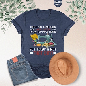 May include: A navy blue t-shirt with a sewing machine and fabric design. The text on the shirt reads "There may come a day when I decide I own too much fabric but today is not that day!"