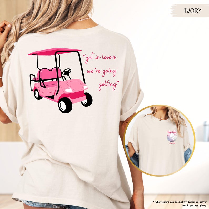May include: Ivory t-shirt with a pink golf cart graphic and the text "get in losers we're going golfing." A small golf ball with a pink bow is on the front pocket. The shirt has a relaxed fit and is made of soft material.
