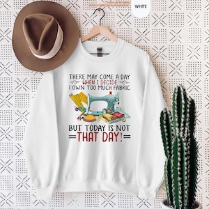 May include: White sweatshirt with a sewing machine and fabric design. The text reads "There may come a day when I decide I own too much fabric but today is not that day!"