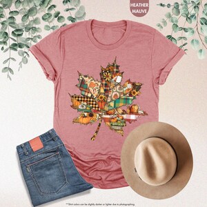 Puede incluir: Una camiseta de manga corta color malva jaspeado con un gr&aacute;fico de hoja de arce compuesto por varios patrones oto&ntilde;ales, incluyendo cuadros, calabazas y girasoles. La prenda se muestra junto a unos vaqueros azules y un sombrero de color canela.