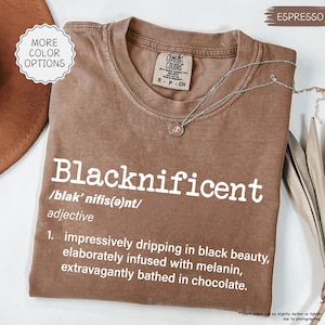May include: A brown t-shirt with the word "Blacknificent" defined as "impressively dripping in black beauty, elaborately infused with melanin, extravagantly bathed in chocolate."