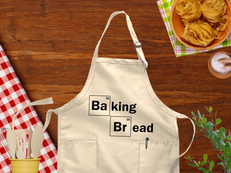 May include: A white apron with a pocket and two black squares with the text "Baking" and "Bread" with the chemical symbols and atomic numbers for the elements Barium and Bromine.
