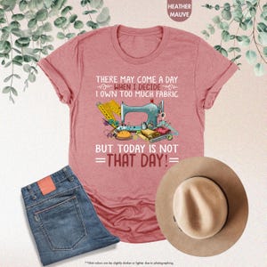May include: Heather mauve t-shirt with a sewing machine and fabric design. The text on the shirt reads "There may come a day when I decide I own too much fabric but today is not that day!"